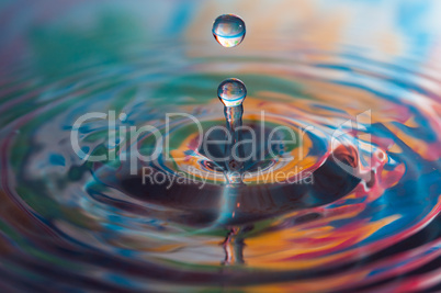 Macro photo of water drops falling into a pool of water, causing a splash and ripples.