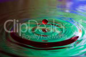 Macro photo of water drops falling into a pool of water, causing a splash and ripples.