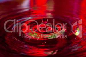 Macro photo of water drops falling into a pool of water, causing a splash and ripples.