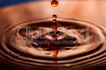 Macro photo of water drops falling into a pool of water, causing a splash and ripples.