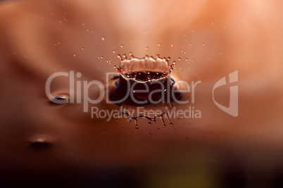 Macro photo of water drops falling into a pool of water, causing a splash and ripples.