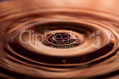 Macro photo of water drops falling into a pool of water, causing a splash and ripples.