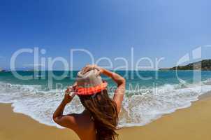 Young girl holding her hat on sandy beach