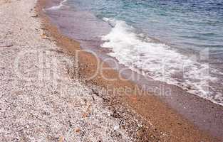 Beach of coarse sand and stones with wave.