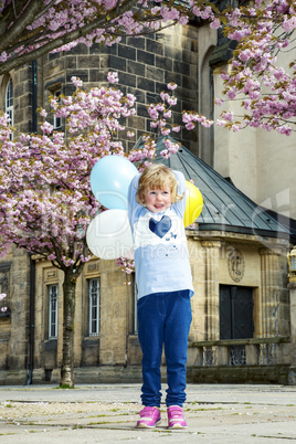 Child playing in the city under blossoming cherry trees with Balloon