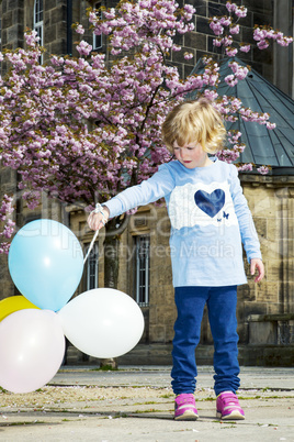 Child playing in the city under blossoming cherry trees with Balloon