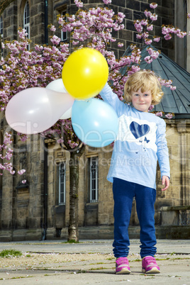 Child playing in the city under blossoming cherry trees with Balloon