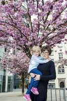 Woman holding toddler in her arms under blossoming cherry trees