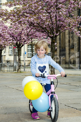 Child with bicycle and balloon in the city under blossoming cherry trees