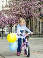 Child with bicycle and balloon in the city under blossoming cherry trees