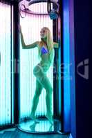 Image of leggy blonde tans in tanning booth