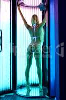 Rear view of slender blonde tans in tanning booth