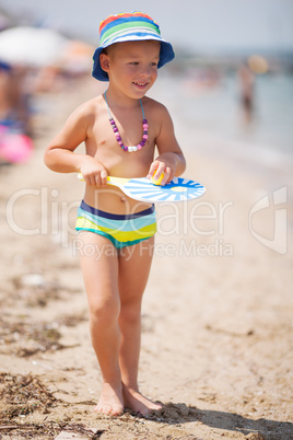 Lovely smiling bot in hat walking on sandy beach