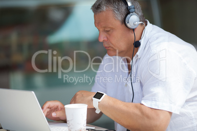 Elderly man typing on laptop in cafe