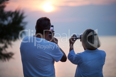 Back view of couple taking photos of sunset