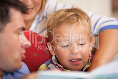Cute little boy reading a book with his parents