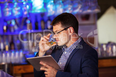 Businessman with tablet drinking whisky in bar