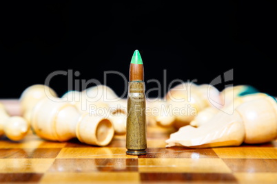 Closeup photo of one bullet standing on chessboard among lying chess pieces.
