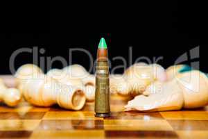 Closeup photo of one bullet standing on chessboard among lying chess pieces.