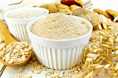 Flour oat in white bowl with flakes in spoon on board