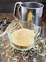 Flour sesame in cup with sieve on dark board