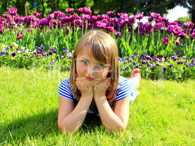 school girl lays on the grass and besides tulips