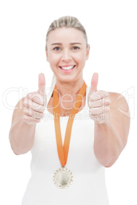 Female athlete wearing a medal and showing thumbs up