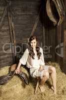 Young woman with horse saddle in the barn