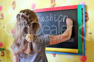 girl with nice plaits writes word Fashion on blackboard