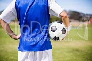 Mid section of female football player standing with a ball