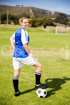 Portrait of female football player standing with her feet on bal