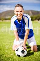 Female football player kneeling on field with ball