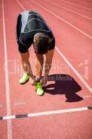 Male athlete tying his shoe laces on running track
