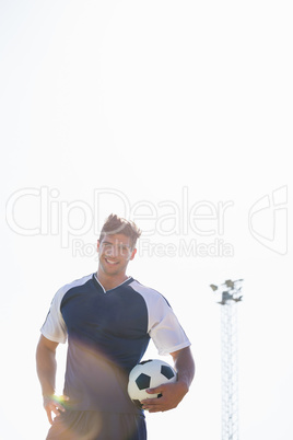 Happy football player standing with a ball