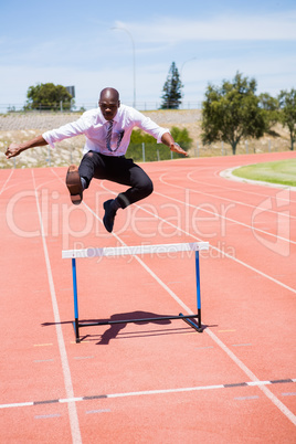 Businessman jumping a hurdle while running