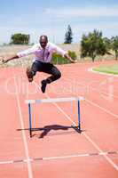 Businessman jumping a hurdle while running
