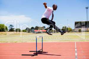 Businessman jumping a hurdle while running