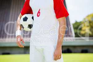 Mid section of football player standing with a ball