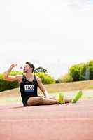 Tired athlete sitting on the running track and drinking water