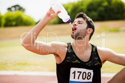 Tired athlete sitting on the running track and drinking water