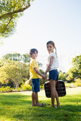 Children holding their hands looking back while holding a luggag