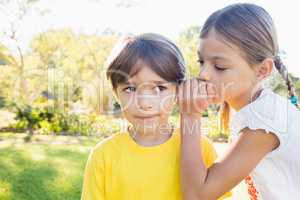 Girl telling a secret in the ear of a little boy in a park