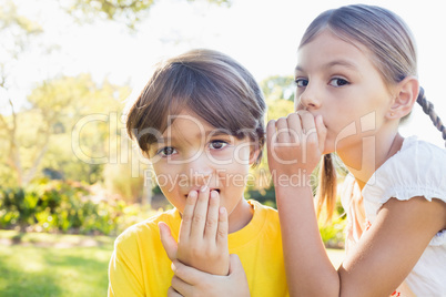 Girl telling a secret in the ear of a little boy