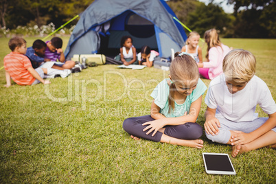 Smiling children are looking their tablet with other children be