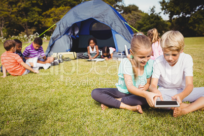 Smiling children are looking their tablet with other children be