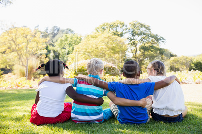 Kids are sitting on the grass together during a sunny day