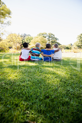 Kids are sitting on the grass together during a sunny day