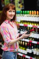 Smiling woman standing with a bottle of wine and posing