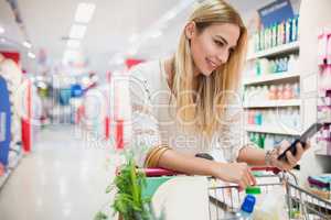 Smiling customer watching her phone at supermarket
