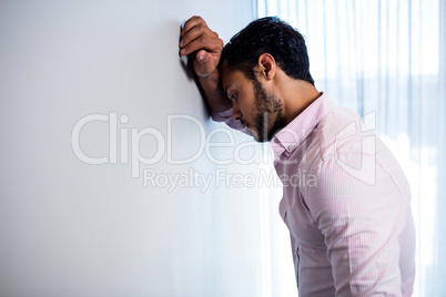 Thoughtful young businessman standing against  wall